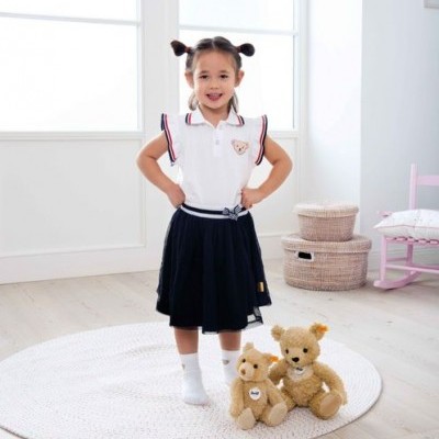 Menina com roupa branca e preta junto a ursinhos de pelúcia num quarto claro