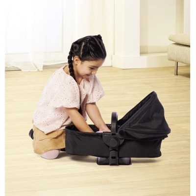 Criança a brincar com carrinho de boneca preto no chão de madeira