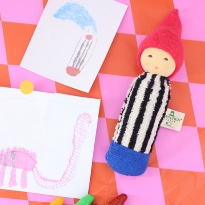 Boneco de tecido com roupa às riscas e chapéu vermelho sobre superfície quadriculada com desenhos infantis