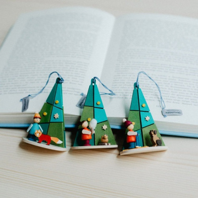 Enfeites de árvore de Natal em madeira com figuras e cordões azuis sobre mesa clara e livro aberto ao fundo