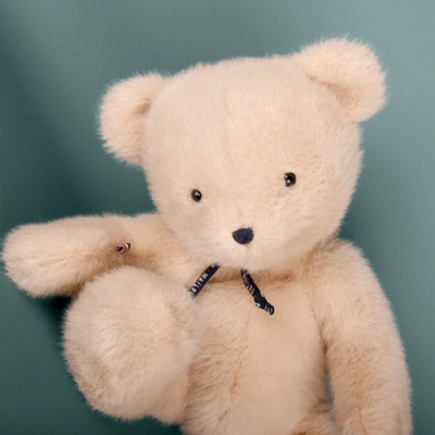 Ursinho de peluche bege com fita preta ao pescoço