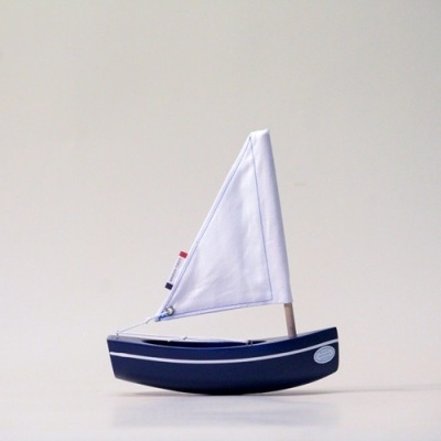 Barco de vela decorativo azul com velas brancas sobre superfície clara