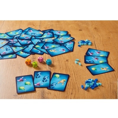Jogo de cartas aquáticas com dados coloridos e peças de madeira azuis sobre mesa de madeira clara.