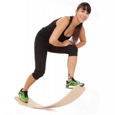 Mulher com roupas desportivas e sapatilhas verdes numa prancha de equilíbrio de madeira