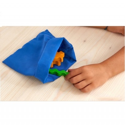 Mão de criança a tocar peça de brinquedo verde saindo de saco azul sobre mesa de madeira
