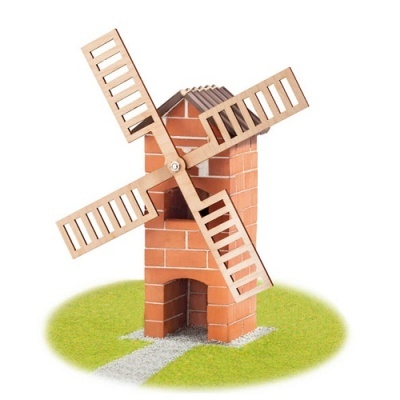 Miniatura de moinho de vento de madeira com desenho de tijolos e pás recortadas sobre base verde.