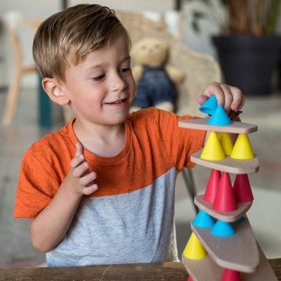 Menino a brincar com jogo de empilhar cones coloridos e placas de madeira.
