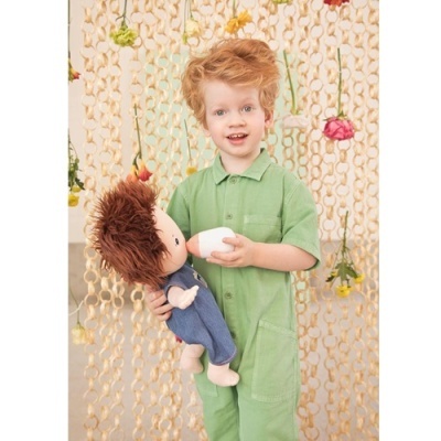 Criança com macacão verde e boneco de pano segurando uma mamadeira