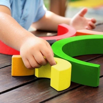 Criança a segurar peça amarela de madeira colorida em cima de mesa de madeira