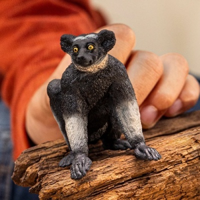 Miniatura de lémure preto e branco com olhos amarelos sobre madeira