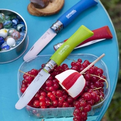 Três facas coloridas OPINEL com groselhas vermelhas e pirulito sobre mesa azul