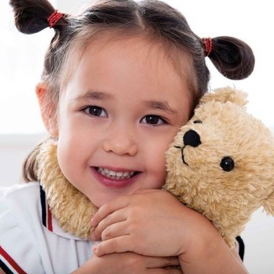 Criança feliz abraçando urso de pelúcia amarelo com etiqueta