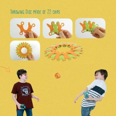 Disco para atirar de 22 peças verdes e laranjas, duas crianças a brincar com ele sobre fundo amarelo