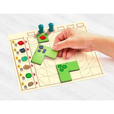 Peças de jogo de tabuleiro verdes com casas e árvores numa mesa clara