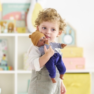 Criança loira segurando boneca negra com roupa azul e gorro castanho