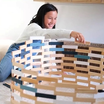 Menina a brincar com tábuas de madeira KAPLA empilhadas.