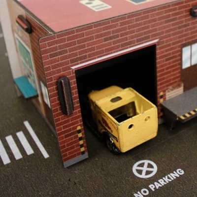Modelo em miniatura de edifício com veículo amarelo saindo da garagem
