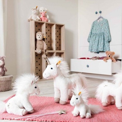 Quatro peluches de unicórnio brancos com crinas cor-de-rosa sobre tapete cor-de-rosa em quarto infantil
