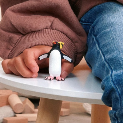 Imagem de figura pequena de pinguim em mesa branca com mão infantil ao lado.