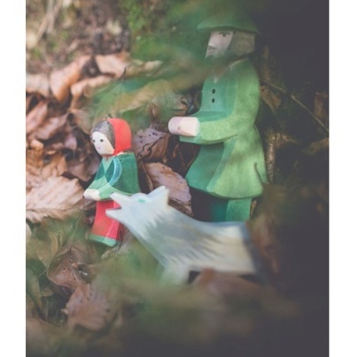 Figuras de madeira pintadas representando pessoas e um lobo em ambiente natural com folhas.