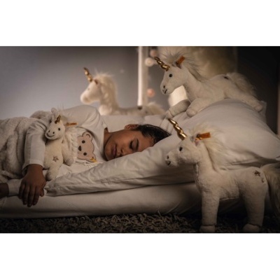 Criança a dormir numa cama com peluches de unicórnio brancos com cornos dourados