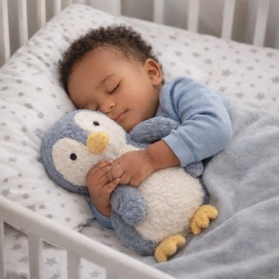 Criança a dormir abraçada a peluche de pinguim numa cama branca com roupa de cama cinzenta com estrelas