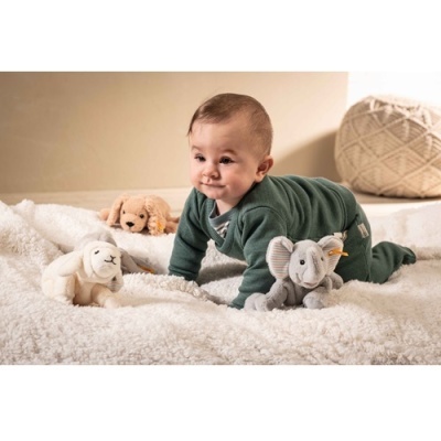Bebé com macacão verde escuro em tapete peludo creme com três peluches de animais