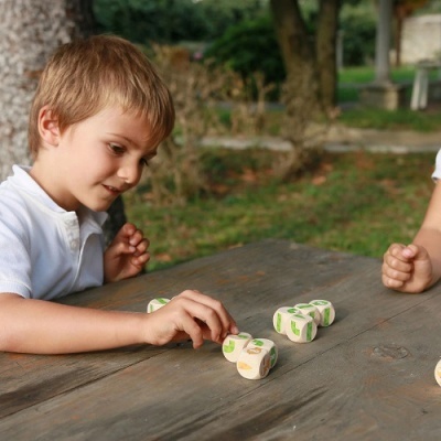 Criança a jogar com dados de madeira coloridos numa mesa de madeira ao ar livre