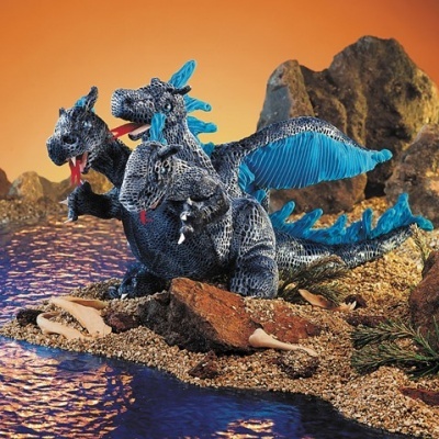 Figura de dragão tricefálico azul e cinzento numa praia rochosa