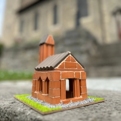 Miniatura de casa feita com blocos de tijolos vermelhos com telhado cinza e base verde