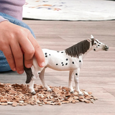 Brinquedo de cavalo branco com manchas pretas segurado na mão de uma criança