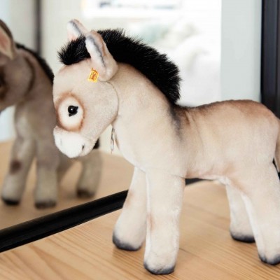 Brinquedo de pelúcia em forma de burro com crina negra em cima de mesa de madeira com espelho ao fundo