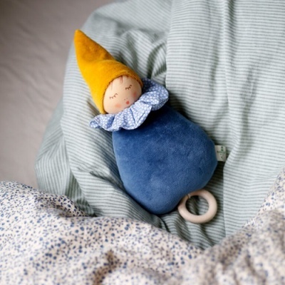 Boneco de peluche gnomo com chapéu amarelo e corpo azul sobre roupa de cama