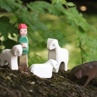 Bonecos em madeira pintada representando figura humana, ovelhas brancas e porco castanho sobre musgo