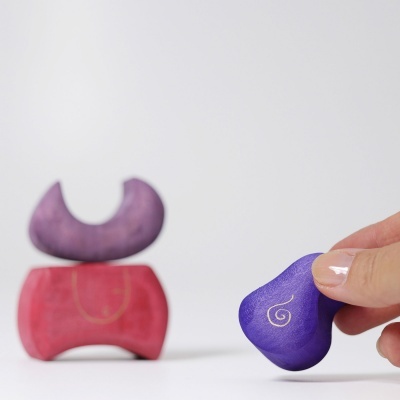 Três blocos coloridos empilháveis, com padrão espiral dourado na peça roxa segurada por uma mão