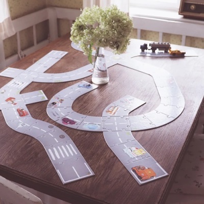 Quebra-cabeças estrada com desenhos de veículos em mesa de madeira e flor em vaso de vidro