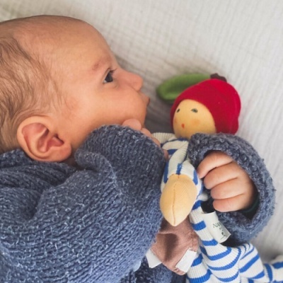 Bebé com camisola azul segurando brinquedo de pano listrado