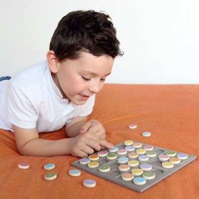 Menino a jogar jogo de tabuleiro com peças circulares coloridas em fundo alaranjado