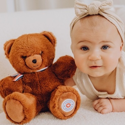 Urso de pelúcia castanho com laço e bebé com laço bege num fundo branco acolchoado
