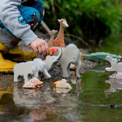 Brinquedos de animais de madeira próximos a água com criança a brincar