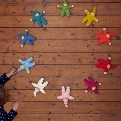 Onze bonecos de peluche coloridos em círculo sobre chão de madeira com crianças a tocar