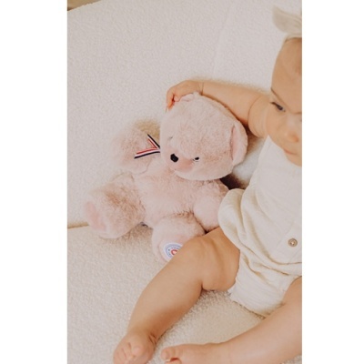 Urso de peluche cor de rosa claro com fita às riscas e bebé vestido de branco