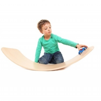 Menino sentado em tábua de madeira curva a brincar com carrinho azul.