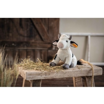 Pelúcia de vaquinha branca e preta sobre mesa de madeira com palha