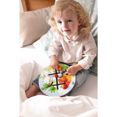 Criança a brincar com brinquedo de madeira colorido numa cama com almofadas.