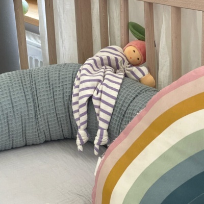 Cama de bebé com almofada colorida arco-íris e boneca de tecido com roupa riscada