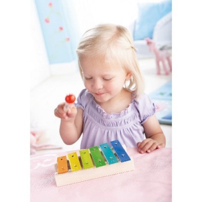 Criança com vestido lilás a tocar xilofone colorido numa mesa rosa em quarto infantil