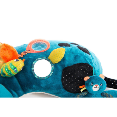 Almofada de pelúcia azul com círculos pretos e acessórios coloridos, incluindo espelho e brinquedo pequeno