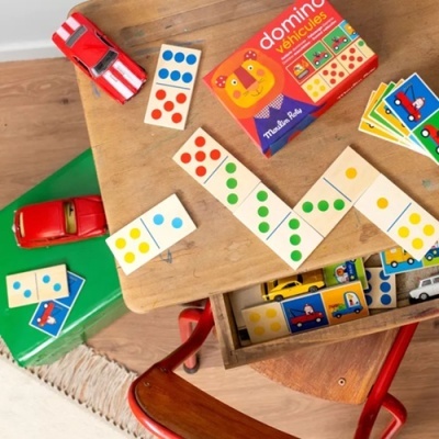 Jogo de dominó infantil de madeira com peças coloridas e carros de brinquedo vermelhos sobre uma mesa de madeira