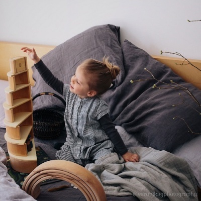 Menina numa cama a brincar com blocos de madeira e arco de madeira.